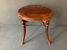 an old wooden table with two legs and a small round top on one end, sitting against a white wall