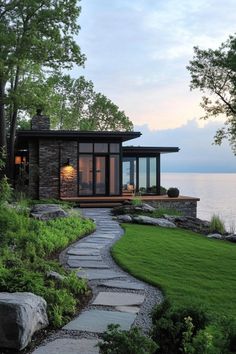 a house that is next to the water with grass and rocks in front of it