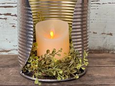 a lit candle in a tin can with some plants growing out of the bottom and inside