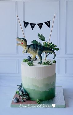 a dinosaur cake is decorated with green and white frosting, while flags are hanging above it