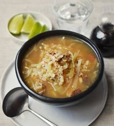 a white plate topped with a bowl of soup next to a spoon and lime wedges