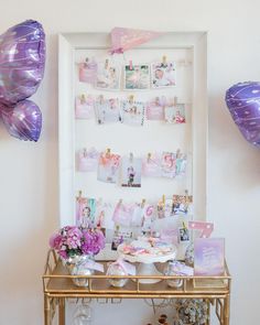 a gold table topped with lots of pink and purple balloons next to a white wall