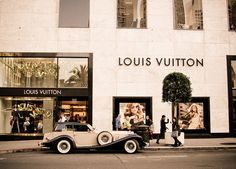 an old car is parked in front of a louis vuitton store on the street