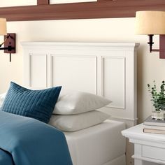 a white bed with blue sheets and pillows next to a night stand on a table