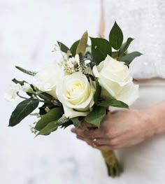 a bride holding a bouquet of white roses and greenery in her hands, close up