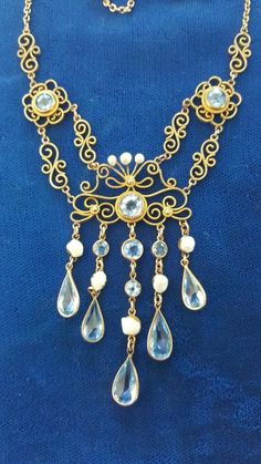 This neckclace is so drippy and ornate! It is gold filled and is 17 inches long. The central fancy part is 4 1/2 inches wide and 2 1/2 inches long. The aqua pastes are all bezel set and the river pearls are all natural. This is a real beauty. C 1890 and American. Follow me on instagram@jettesjewels. Antique Gold Dangle Necklaces, Heirloom Gold Necklace With Jewels, Antique Gold Baroque Necklaces, Antique Gold Baroque Necklace, Victorian Gold Necklace With Jewels, Gold Pendant Necklace With Historical Design, Festoon Necklace, River Pearls, Jewelry Techniques