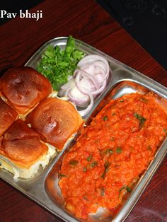 a metal tray filled with food on top of a wooden table next to an onion bun