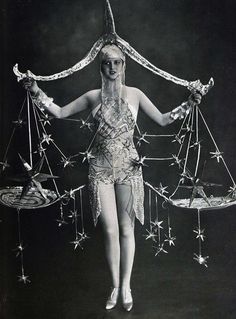 a woman is holding two scales with stars around her body and wearing white high heels