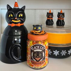 three black cats sitting on top of a counter next to jars with candy in them