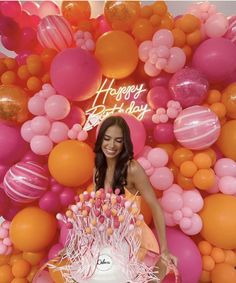 a woman standing in front of a cake surrounded by balloons and streamers with the words happy birthday written on it