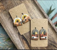 two earrings with sunflowers on them are sitting on a piece of cardboard next to a card