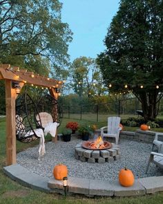 an outdoor fire pit surrounded by chairs and lights with pumpkins on the ground next to it