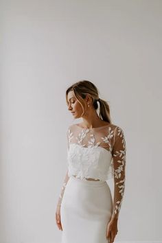 a woman wearing a white wedding dress with sheer sleeves