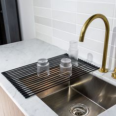 a kitchen sink with two glasses sitting on the counter next to it and a gold faucet