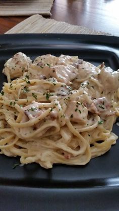 a black plate topped with pasta covered in sauce