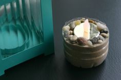 a candle that is sitting in a jar with rocks and pebbles on the table next to it