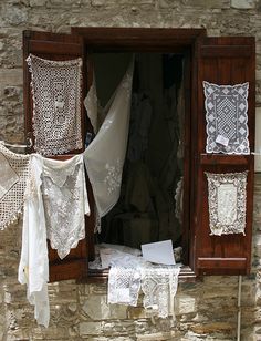 an old window with white lace hanging from it's sides and clothes hung to dry