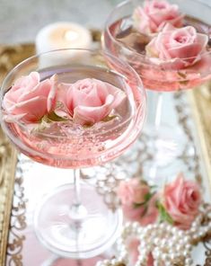 two wine glasses with pink roses in them on a gold and white table cloth next to candles