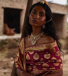 a woman in a red and gold sari standing next to a pole with her hands on her hips