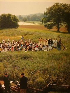 a large group of people standing on top of a lush green field next to trees