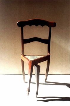 a wooden chair sitting on top of a white floor next to a wall with a shadow cast on it