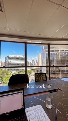 an office desk with a laptop and papers on it in front of large windows overlooking the city