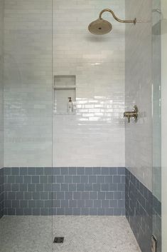 a walk in shower sitting next to a white tiled wall and floor covered in blue tiles