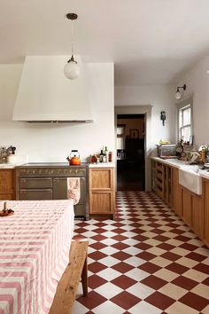 a large kitchen with checkered flooring and wooden cabinets, an oven hood over the stove