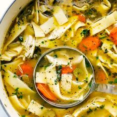 a ladle full of chicken noodle soup with carrots and celery