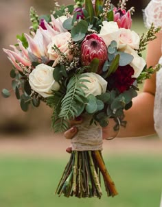 a bride holding a bouquet of flowers in her hand with greenery on the side