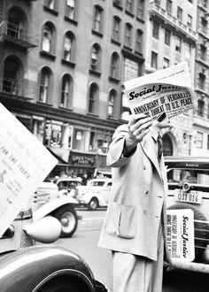 a woman standing in the street reading a newspaper