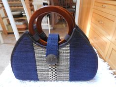 Lovely Vintage Wooden Handled handbag from the 70's. Navy Blue in color with straw- like weave and contrasting black threading. A large 1 1/2 button adorns the frontal closure snap which has UK1519246 Patent on the metal snap. This purse is flat bottomed which makes it sit so nice. I have not found any tag or make for this bag, but it is in like new condition. Length: 8 inches Width: 12 inches Deep: 4 inches Acrylic Bag, Woven Bags, Woven Handbags, Frontal Closure, Top Handle Bags, Woven Bag, Wooden Handles, Purses And Handbags, Straw Bag