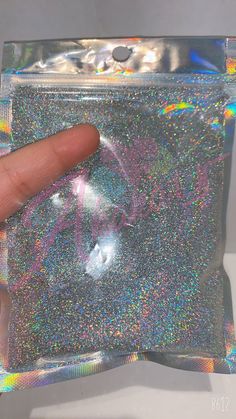 a hand is pointing at a holographic bag that has been filled with glitter