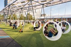 people are sitting on swings in the grass at an open air park with large white circles hanging from them