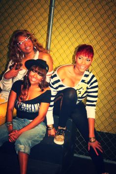 three women posing for the camera in front of a fence