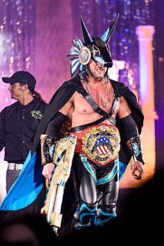 a man in a wrestler outfit walking on stage with an american flag belt around his waist