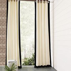 an open window with black and white curtains in front of brick wall next to potted plant