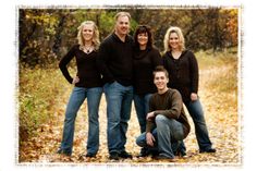 a group of people posing for a picture in front of some trees with leaves on the ground