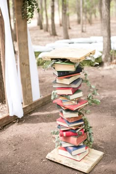 a tall stack of books sitting on top of a wooden stand in the woods next to trees