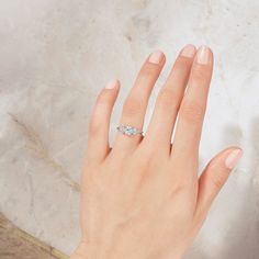 a woman's hand with a diamond ring on top of her left hand, against a marble background