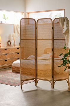 a room divider made out of bamboo with a plant in the foreground and a bed behind it