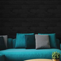 a teal couch with pillows on it in front of a wooden table and black wall