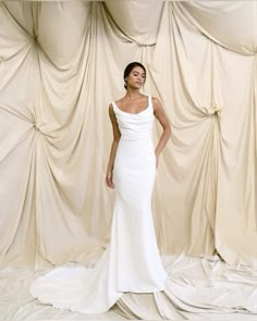 a woman standing in front of a backdrop wearing a white dress