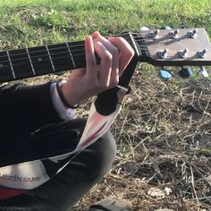 a person sitting on the ground with a guitar in their hand and grass behind them