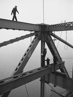 a man standing on top of a tall metal structure next to the ocean in black and white