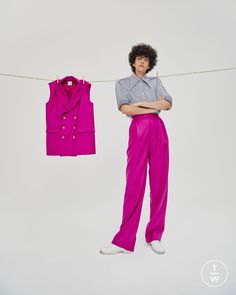 a man standing next to a pink shirt and purple pants on a clothes line with his arms crossed