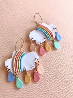 three pairs of earrings with rainbows and clouds hanging from them on a pink surface