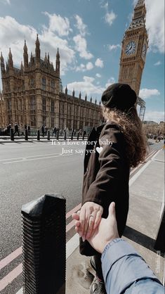 two people holding hands on the side of a road with big ben in the background