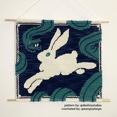 a blue and white wall hanging with an image of a rabbit on it's back