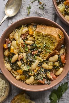 two bowls filled with beans and greens next to bread